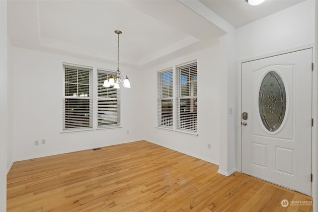 entrance foyer with an inviting chandelier, light wood-type flooring, and a tray ceiling