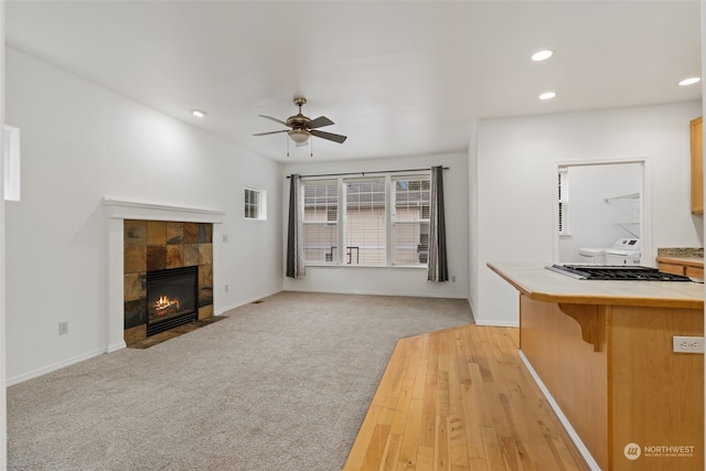 kitchen with ceiling fan, tile countertops, a breakfast bar area, a tiled fireplace, and light carpet