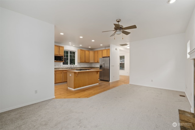 kitchen featuring a breakfast bar, a center island, ceiling fan, light colored carpet, and stainless steel fridge with ice dispenser