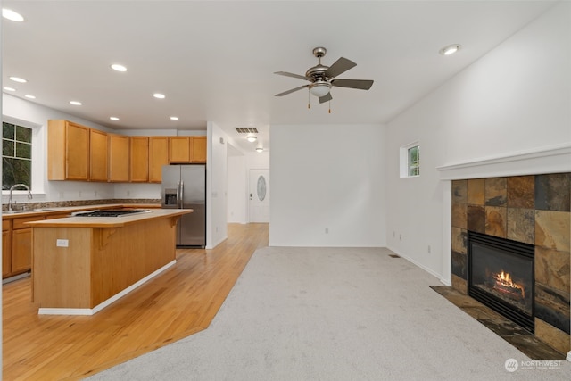 kitchen with stainless steel fridge, a kitchen breakfast bar, light hardwood / wood-style floors, a kitchen island, and a tiled fireplace