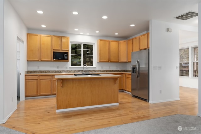 kitchen featuring stainless steel fridge with ice dispenser, a center island, light hardwood / wood-style floors, and black microwave