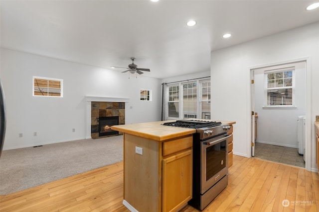 kitchen with high end range, ceiling fan, a tile fireplace, light hardwood / wood-style flooring, and tile counters