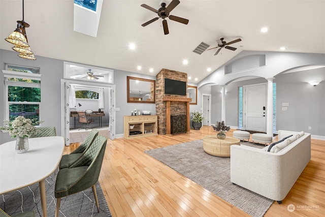 living room with ornate columns, ceiling fan, high vaulted ceiling, light hardwood / wood-style floors, and a fireplace