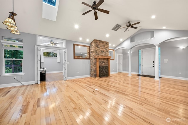 unfurnished living room with light wood-type flooring, decorative columns, ceiling fan, high vaulted ceiling, and a stone fireplace