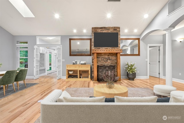 living room with hardwood / wood-style floors, a stone fireplace, lofted ceiling, and ornate columns