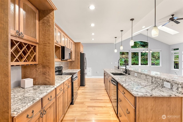 kitchen with light stone countertops, appliances with stainless steel finishes, vaulted ceiling with skylight, sink, and light hardwood / wood-style flooring