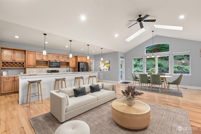 living room featuring a skylight, ceiling fan, sink, light hardwood / wood-style flooring, and high vaulted ceiling