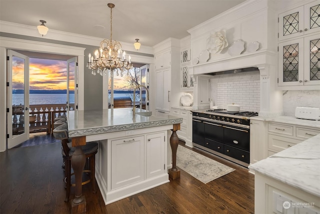 kitchen with dark wood-type flooring, decorative light fixtures, an island with sink, tasteful backsplash, and white cabinets