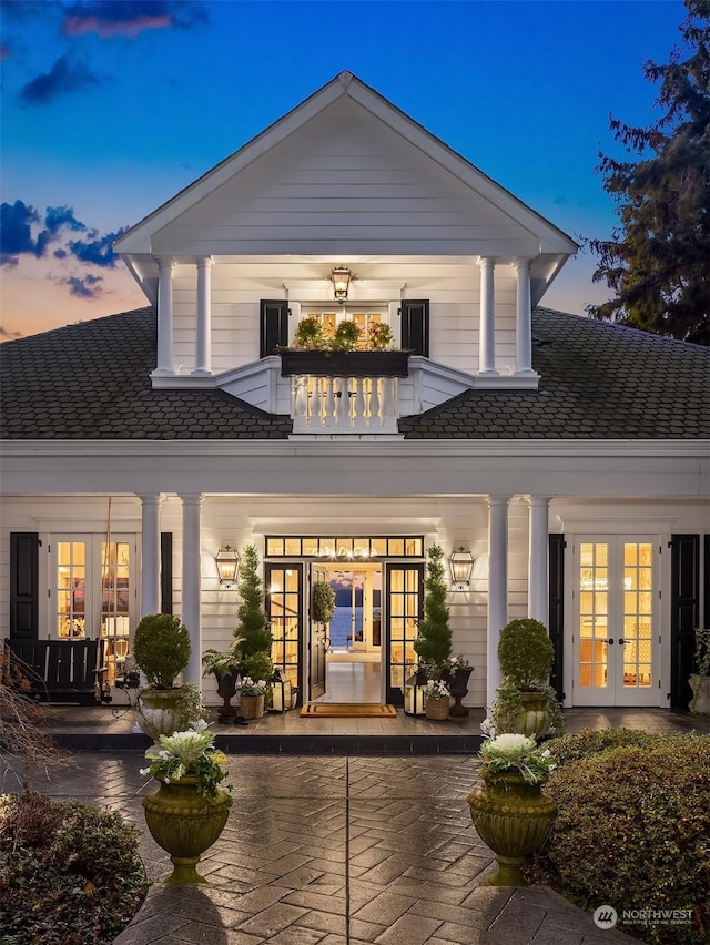 back house at dusk with french doors and a balcony