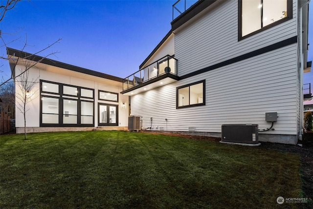 back house at dusk featuring a yard, central AC, and a balcony