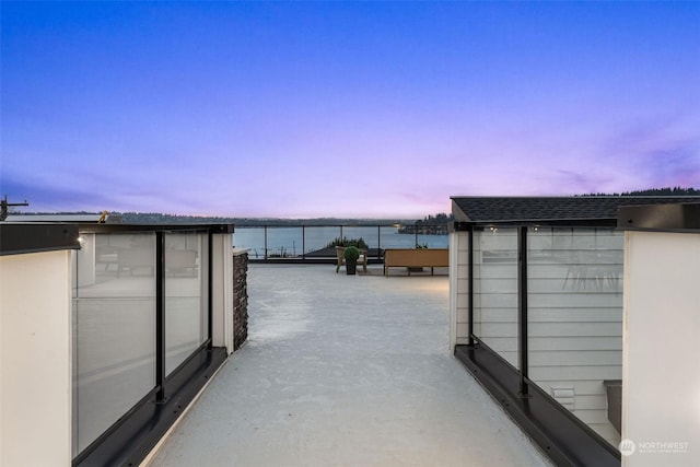 patio terrace at dusk featuring a water view and a balcony