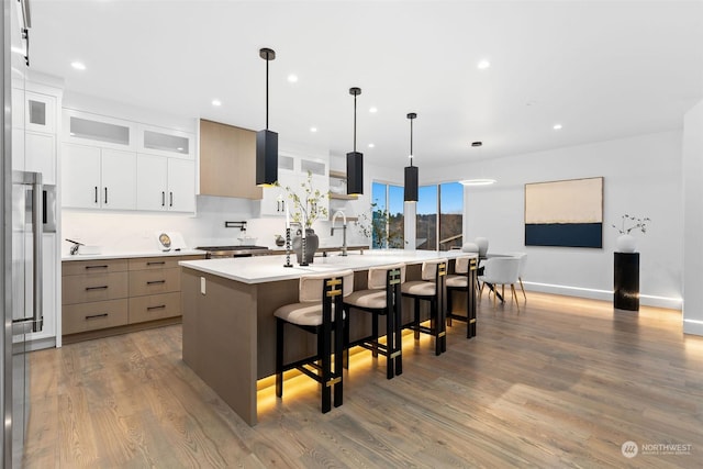 kitchen with white cabinetry, an island with sink, pendant lighting, wood-type flooring, and a breakfast bar