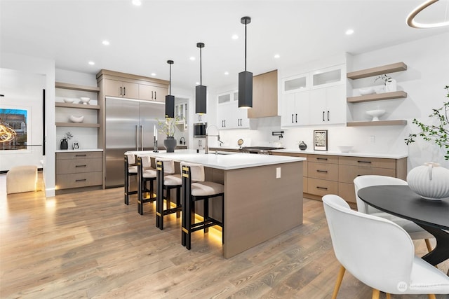 kitchen with a large island, sink, light hardwood / wood-style flooring, decorative light fixtures, and appliances with stainless steel finishes