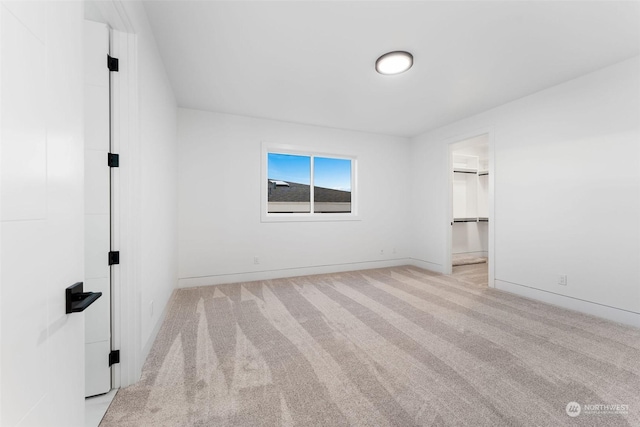 unfurnished bedroom featuring a walk in closet and light colored carpet