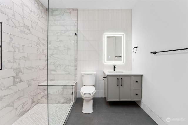 bathroom with vanity, tile patterned floors, toilet, tiled shower, and tile walls