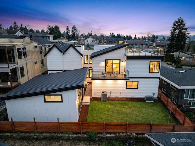 back house at dusk with a balcony, central AC unit, and a lawn