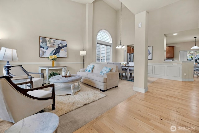 living area featuring a chandelier, a high ceiling, light wood-type flooring, and a decorative wall