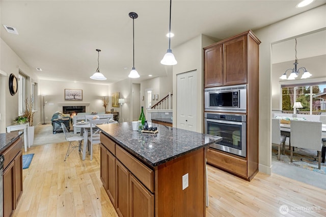 kitchen featuring appliances with stainless steel finishes, a center island, light wood-style floors, and a lit fireplace