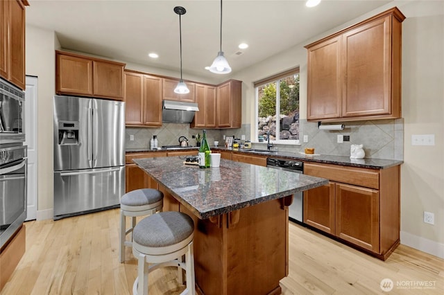 kitchen with appliances with stainless steel finishes, a sink, light wood finished floors, and a kitchen bar