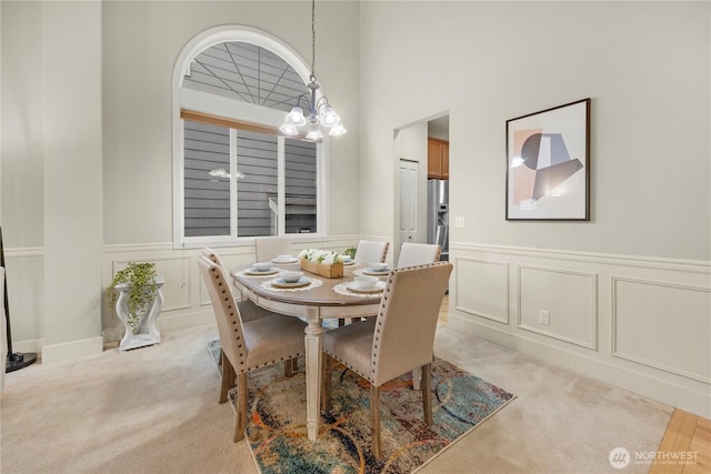 dining area with light colored carpet, a decorative wall, and an inviting chandelier