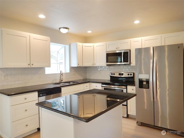 kitchen with light wood-type flooring, stainless steel appliances, a kitchen island, sink, and white cabinetry