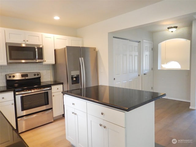 kitchen with decorative backsplash, white cabinets, stainless steel appliances, and a kitchen island