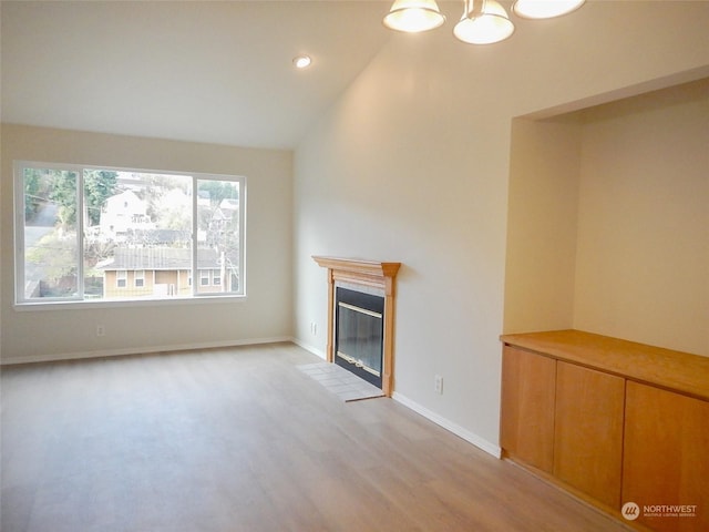 unfurnished living room with light hardwood / wood-style floors, lofted ceiling, and an inviting chandelier