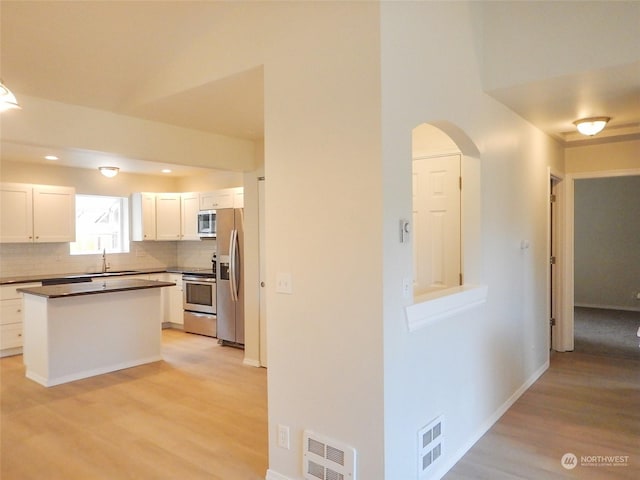 kitchen with backsplash, white cabinets, sink, appliances with stainless steel finishes, and light hardwood / wood-style floors