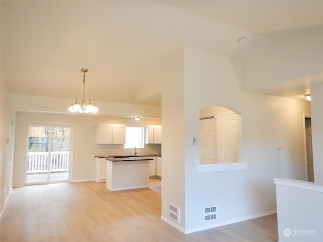 kitchen featuring backsplash, vaulted ceiling, white cabinets, light hardwood / wood-style floors, and hanging light fixtures