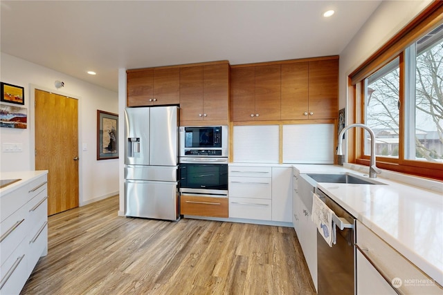 kitchen with stainless steel appliances, sink, light hardwood / wood-style flooring, and white cabinets