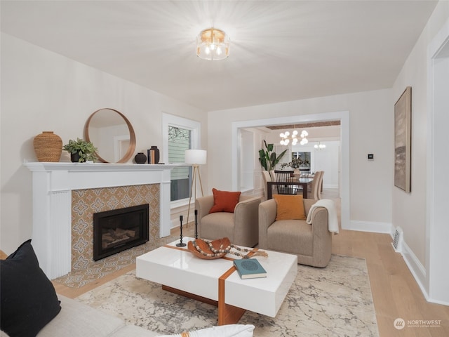 living room with a tiled fireplace, light hardwood / wood-style flooring, and an inviting chandelier