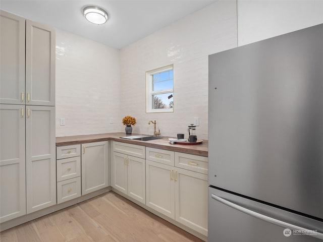 kitchen with stainless steel refrigerator, light hardwood / wood-style floors, wood counters, and sink