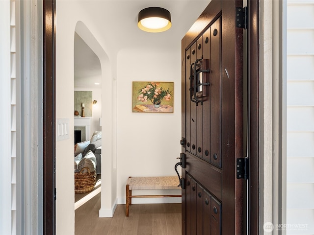 foyer entrance with baseboards, a fireplace, arched walkways, and wood finished floors