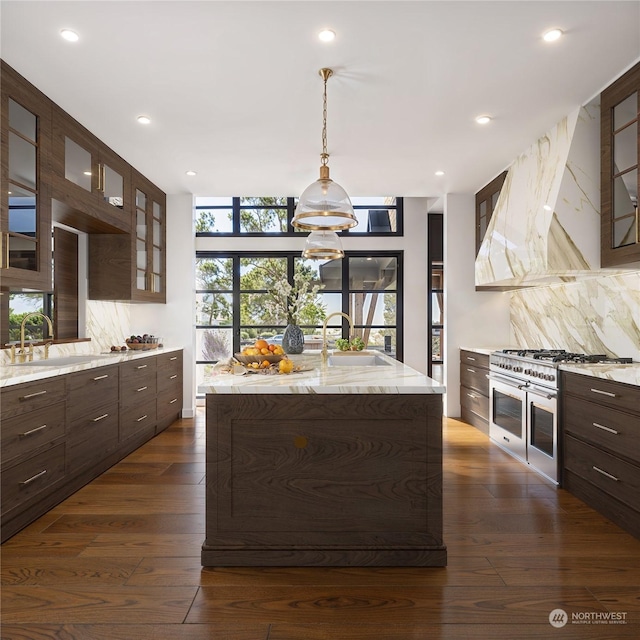 kitchen with double oven range, sink, a center island with sink, and backsplash