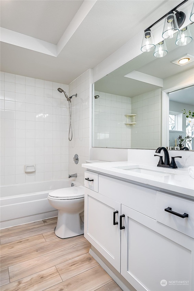 full bathroom with vanity, tiled shower / bath, hardwood / wood-style flooring, and toilet