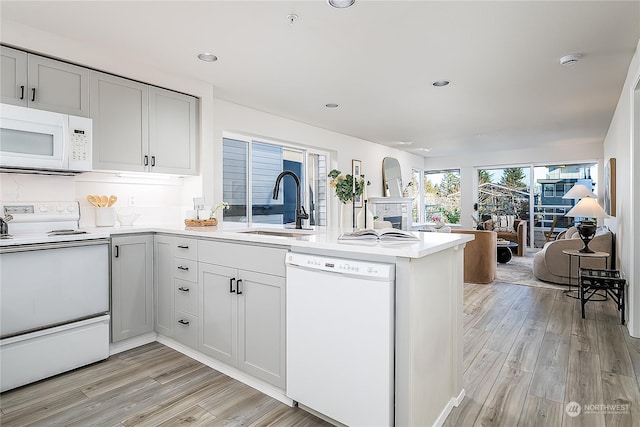 kitchen with sink, kitchen peninsula, white appliances, and light hardwood / wood-style flooring