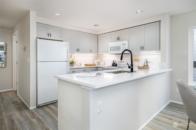 kitchen with white appliances, kitchen peninsula, and light wood-type flooring