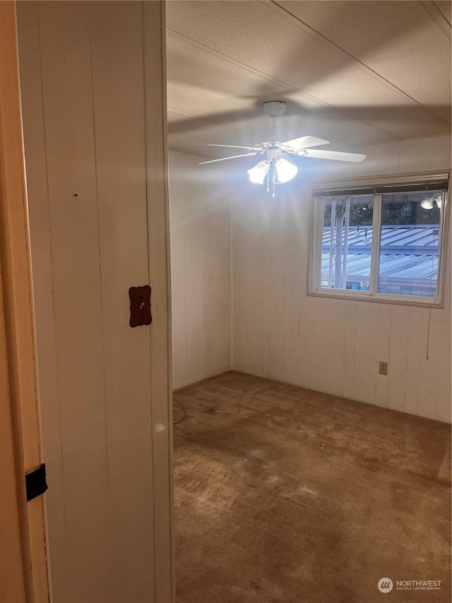 carpeted spare room with wooden walls and ceiling fan