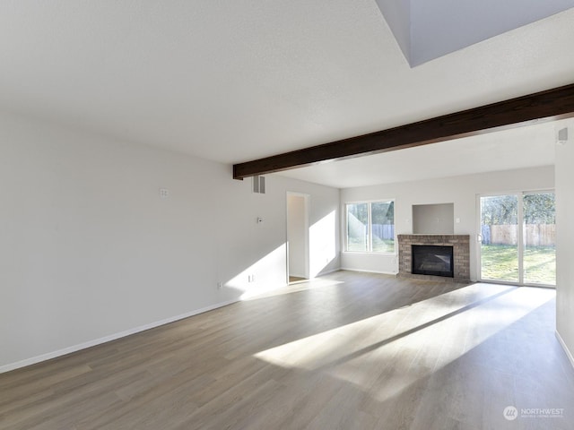 unfurnished living room featuring beamed ceiling, light hardwood / wood-style floors, and a brick fireplace