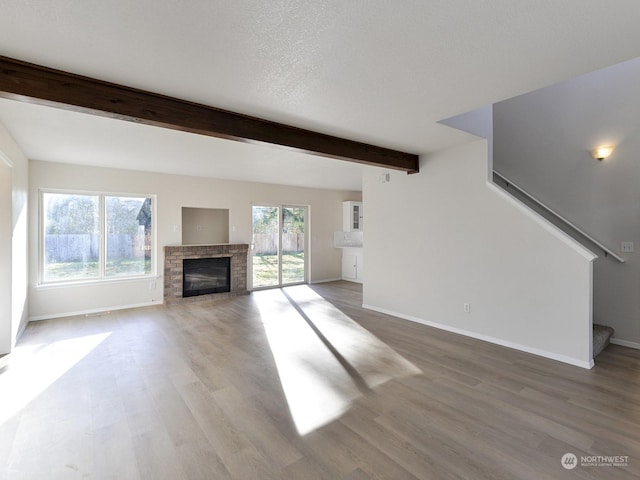 unfurnished living room featuring beamed ceiling, wood-type flooring, and a brick fireplace