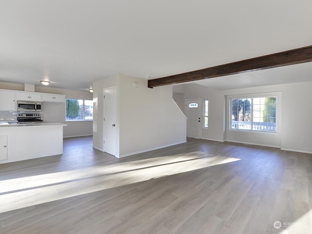 unfurnished living room featuring beam ceiling, light hardwood / wood-style flooring, and a healthy amount of sunlight