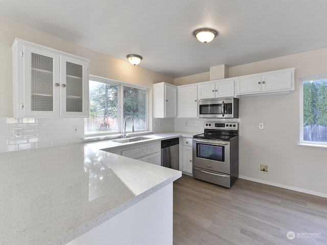 kitchen with kitchen peninsula, appliances with stainless steel finishes, tasteful backsplash, sink, and white cabinets