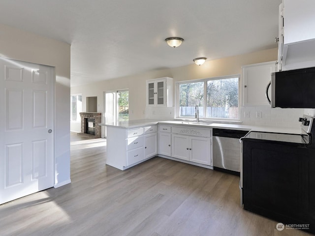 kitchen featuring sink, stainless steel appliances, a brick fireplace, kitchen peninsula, and white cabinets