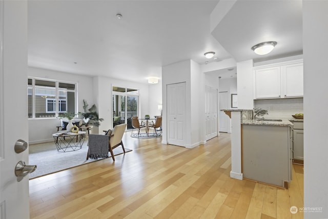 kitchen with sink, white cabinets, decorative backsplash, light hardwood / wood-style floors, and light stone countertops