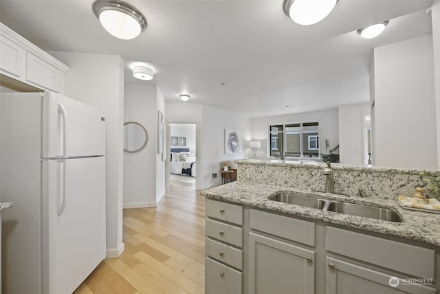 kitchen featuring sink, light wood-type flooring, white fridge, light stone countertops, and white cabinets