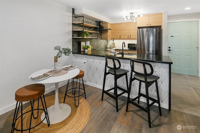 kitchen featuring stainless steel refrigerator, light brown cabinets, a kitchen breakfast bar, kitchen peninsula, and decorative backsplash