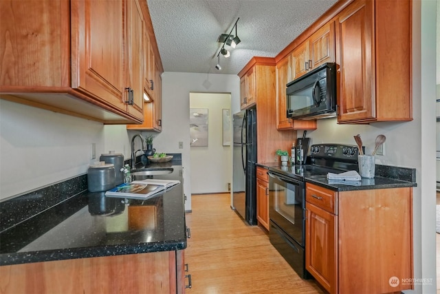 kitchen featuring rail lighting, a textured ceiling, sink, black appliances, and dark stone countertops