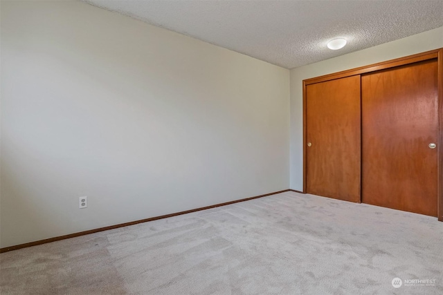 unfurnished bedroom featuring light carpet, a closet, and a textured ceiling