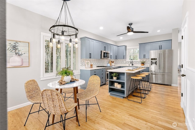 kitchen featuring high end appliances, hanging light fixtures, a center island, tasteful backsplash, and light wood-type flooring