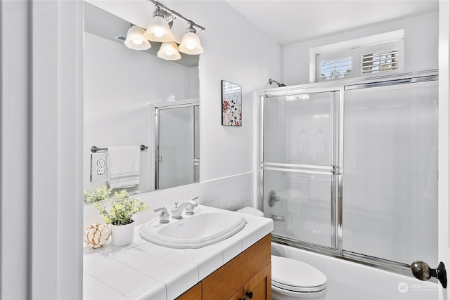 full bathroom featuring combined bath / shower with glass door, vanity, and toilet